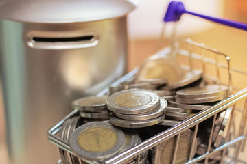 Many coins are in the mini shopping cart with coin bank. Saving money concept.