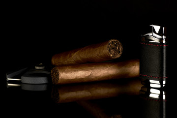 Cigar with cutter and lighter, reflected on a black glass table