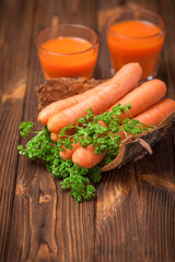 Carrot juice in beautiful glasses, cut orange vegetables and green parsley on dark brown wooden background. Fresh orange drink. Dark mood. Close up photography. Selective focus. Vertical banner