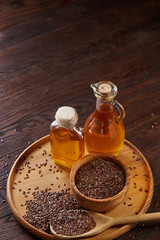 Flax seeds in bowl and flaxseed oil in glass bottle on wooden background, top view, close-up, selective focus