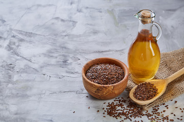 Flax seeds in bowl and flaxseed oil in glass bottle on light textured background, top view,...