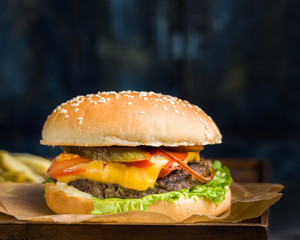 Delicious fresh tasty burger with beef, tomato, cheese, lettuce and french fries served on a wooden cutting board on dark background. Street fast food