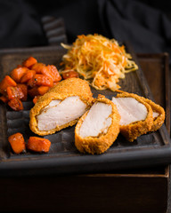Gourmet delicious crispy fried chicken breast (nuggets) with a spicy sauce and served with chopped fresh herbs, caramelized carrots and cabbage salad on an old rustic wooden chopping board