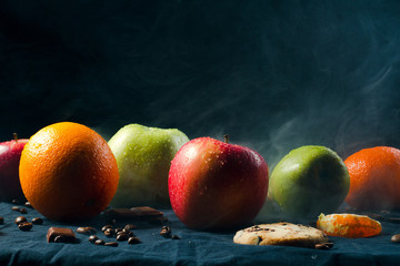 Wet and fresh fruit lie on a black background and in smoke