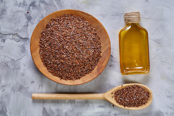 Flax seeds in bowl and flaxseed oil in glass bottle on light textured background, top view, close-up, selective focus