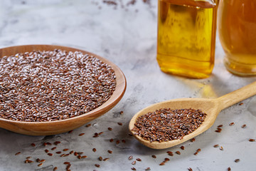 Flax seeds in bowl and flaxseed oil in glass bottle on light textured background, top view, close-up, selective focus
