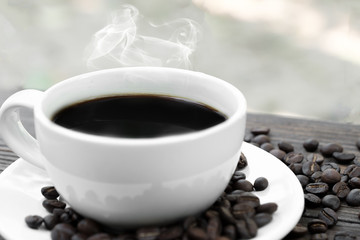Black coffee in white cup surrounded by roast coffee bean.