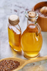 Flax seeds in bowl and flaxseed oil in glass bottle on light textured background, top view,...
