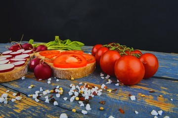 Spread butter on bread with sliced tomatoes and radishes. Fresh snack on natural wooden background