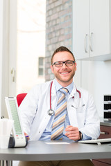 Young doctor sitting in surgery at desk smiling