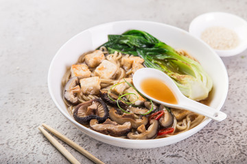 asian vegan noodle soup with tofu cheese,shiitake mushroms and pak choi in white bowl