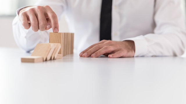 Businessman preventing dominoes from crumbling with finger