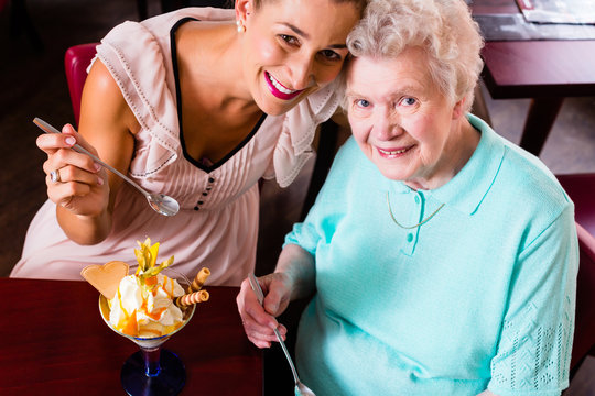 Senior woman and granddaughter having fun eating ice cream sundae in cafe