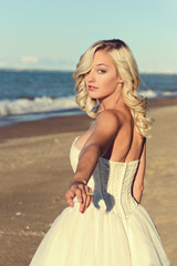 Fototapeta na wymiar blonde woman in white dress follow me on beach
