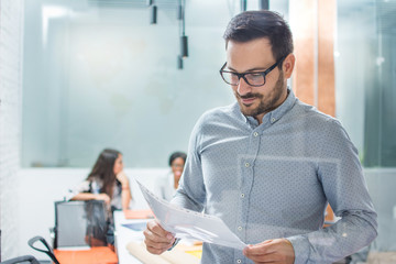 Portrait of busy man wearing glasses and smart casual wear reading documentation in the office.