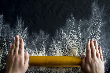 Female hands with a rolling pin on a black background. Free space for text .