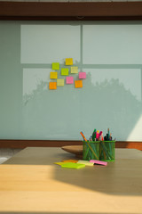 Conference room with colorful writing equipment on wooden desk and note pad on glass wall.