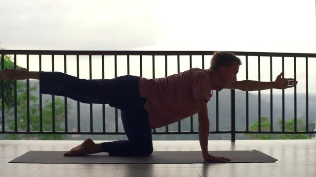 Man practice cat cow yoga pose at balcony at sunrise rapid slow motion
