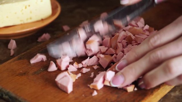 Woman quickly cuts sausage with knife into small pieces on cutting board