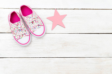 Pink children's sneakers and a pink star on a wooden background. Copy space