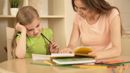 Mother helping daughter with homework, happy smart girl enjoying home education