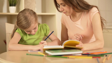 Strict mother watching her daughter doing homework helping her, home education