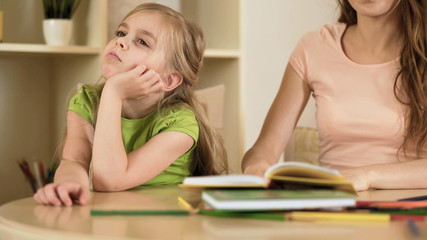 Sensitive mother hopelessly explaining homework to naughty daughter, disregard