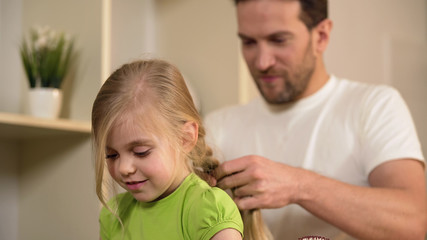 Happy single father braiding daughter's hair, taking care of beloved little girl