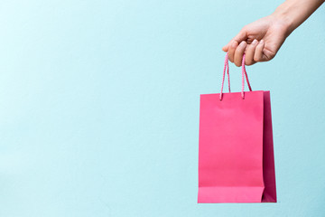 Hand of business woman hold pink shopping bag on blue concrete background