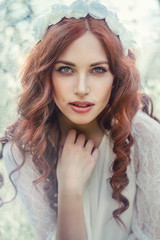 Fototapeta premium Beautiful young woman in white glamour dress with long curly hair in spring flowers bloom