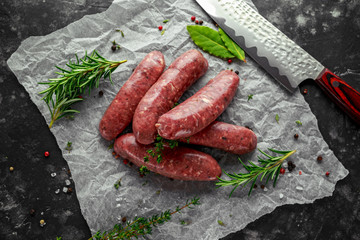 Freshly made raw breed butchers sausages in skins with herbs on crumpled paper.