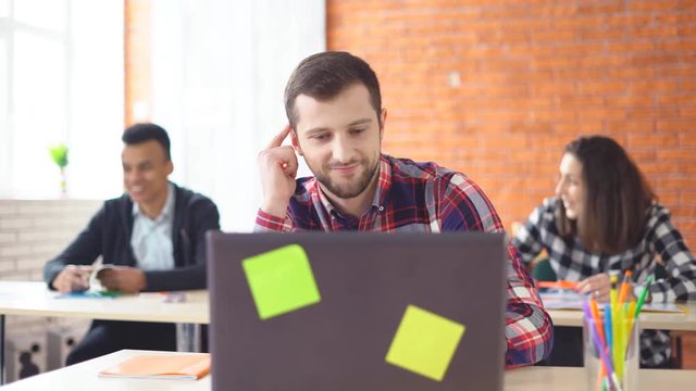 young attractive male student preparing for the exam. reads on the Internet educational information. the man is sitting in front of the computer in the classroom. students learn in the background. 4k