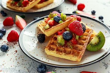 Fresh egg waffles dessert for breakfast with fruits strawberries, blueberries, blackberries, raspberries and kiwi