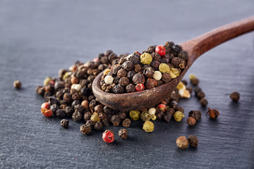 Top view on composition of peppercorns in wooden spoon on dark background, close-up.