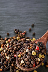 Top view on composition of peppercorns in wooden spoon on dark background, close-up.