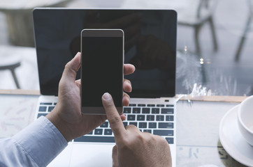 attractive hand of business man using smartphone and laptop working with coffee cup in coffee shop on top view.