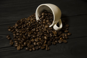 Grains of coffee and a cup on a black, wooden background.