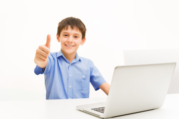 boy in a blue shirt uses a laptop sitting indoors at a table