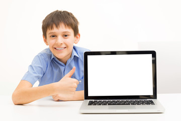 boy in a blue shirt uses a laptop sitting indoors at a table