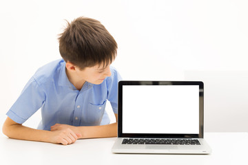 boy in a blue shirt uses a laptop sitting indoors at a table
