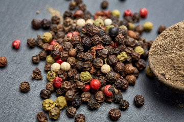 Top view on composition of peppercorns in wooden spoon on dark background, close-up.