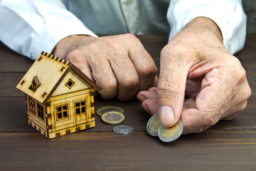 Old man hands and a model home with the coins on the table .The concept of mortgages and Bank loans. Poverty. Rental property. Risk insurance