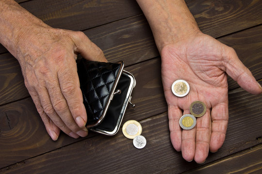  An elderly person holds the coins over the old empty wallet.Hands of beggar with few coins. The concept of poverty in retirement.