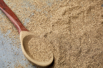 Top view of a wooden spoon full of grind black pepper, shallow depth of field.