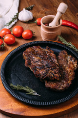 Fried steak with seasonings in an iron plate on a wooden table. tomatoes pepper garlic.