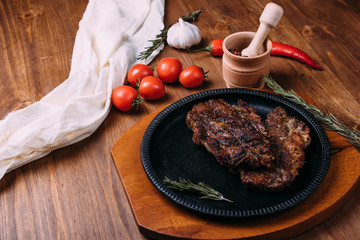 Fried steak with seasonings in an iron plate on a wooden table. tomatoes pepper garlic.