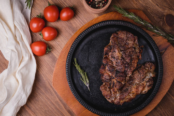 Fried steak with seasonings in an iron plate on a wooden table. tomatoes pepper garlic.