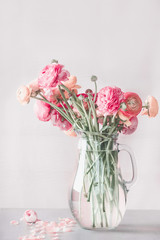 Pastel color ranunculus flowers bunch in glass vase on table, front view