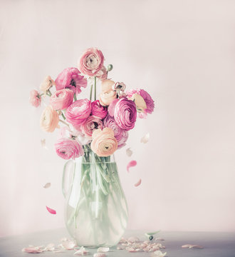 Fototapeta Pastel color ranunculus flowers bouquet with falling petals in glass vase on table, front view