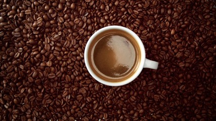 top view of cup of black coffe put it on coffe beans background. White cup of black coffee
